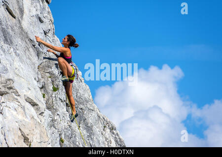 Female rock climber tannées en short jaune sur steep rock face, avec ciel bleu et nuages Banque D'Images