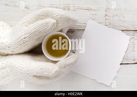 Woman's hands holding gants dans une tasse de thé avec carte vierge sur la table en bois blanc Banque D'Images