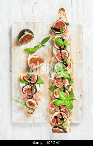 Sandwich baguette longue prosciutto avec viande, fromage mozzarella, roquette, figues et basilic sur planche en bois peint blanc minable ove Banque D'Images