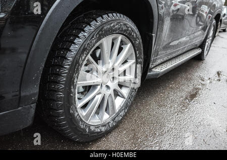 Fragment de suv non identifiables, voiture noire de roues en alliage léger avec des pneus d'hiver sur la route sale Banque D'Images