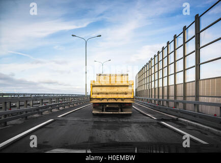 Gros camion benne industrielle jaune va sur route asphaltée, vue arrière d'autres agences de cabin Banque D'Images