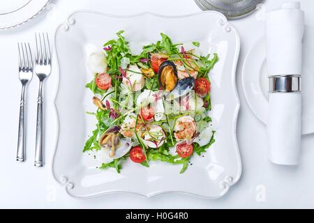 Une salade de fruits de mer avec les palourdes, les crevettes, les calmars, laitue, tomates et fines herbes on white plate Banque D'Images