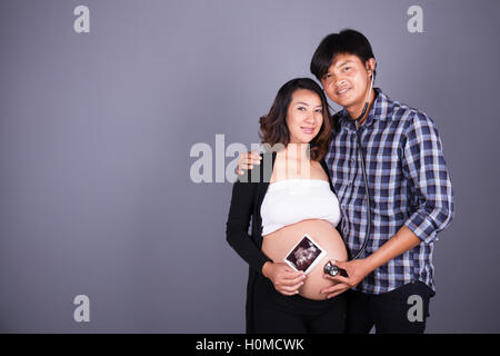 Enceinte et mari heureux avec stéthoscope et image échographique sur fond de mur gris Banque D'Images