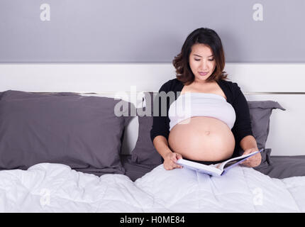 Femme enceinte de lire un livre en position allongée sur un lit dans la chambre à coucher à la maison Banque D'Images