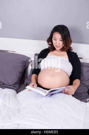 Femme enceinte de lire un livre en position allongée sur un lit dans la chambre à coucher à la maison Banque D'Images