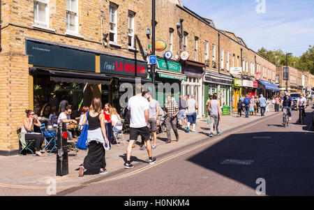 Les gens qui marchent devant les boutiques et restaurants à Broadway market, l'Est de Londres, sur une journée ensoleillée. Banque D'Images