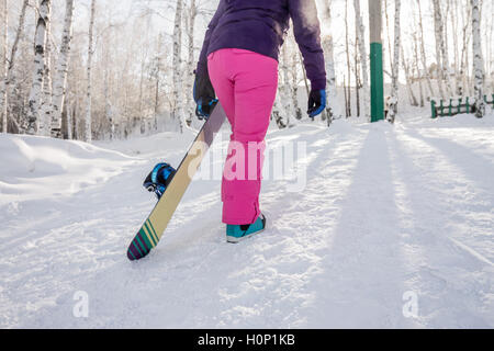 Veste fille en violet et rose avec pantalons snowboard dans les mains de la côte en hiver Banque D'Images