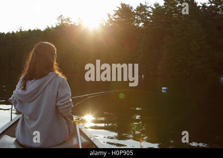 Fille avec la canne à pêche en canoë sur un lac dans le Vermont en tant que le soleil se lève Banque D'Images