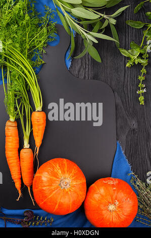Carottes, citrouille, sauge, basilic et thym sur un tableau noir et une serviette bleu top view with copy space Banque D'Images