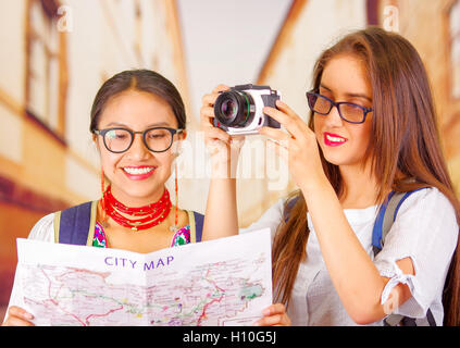 Deux belles jeunes femmes se faisant passer, l'un portant des vêtements traditionnelle des Andes, l'autre dans des vêtements décontractés avec un appareil photo, holding plan de ville d'interaction, à la fois souriant, l'arrière-plan du parc Banque D'Images