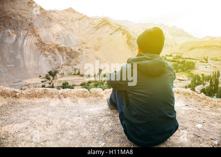 Young male traveler assis sur le sable, falaise, pensez à quelque chose à Leh, Ladakh, Inde Banque D'Images