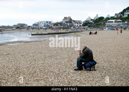 Sac à dos un sans-abri de boire du café assis sur la plage face à la mer à Lyme Regis, dans le Dorset, Angleterre Royaume-uni KATHY DEWITT Banque D'Images