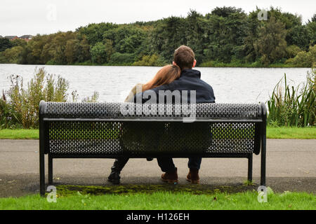 Jeune couple assis sur un banc avec vue sur un lac Banque D'Images