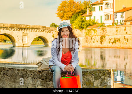 Rimini, Italie, tourisme à maturité avec panier assis sur le quai du port du canal à l'ancien pont romain à l'arrière-plan Banque D'Images