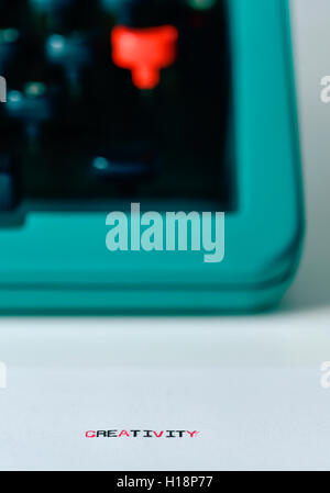 Gros plan de l'terme créativité à la machine dans un livre blanc et une vieille machine à écrire dans l'arrière-plan bleu Banque D'Images