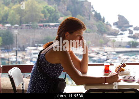 En colère tristesse girl sitting in cafe et feuilletant un téléphone intelligent. Antalya, la vieille ville, paysage Banque D'Images