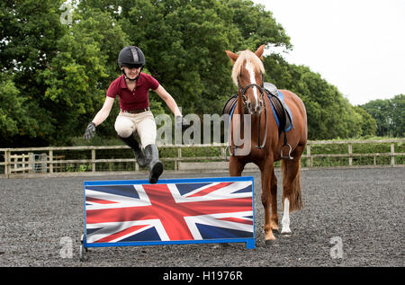 Un jeune cavalier Cheval sautant une clôture basse un poney alezan regarde le cavalier saute une clôture basse montrant le drapeau du Royaume-Uni Banque D'Images