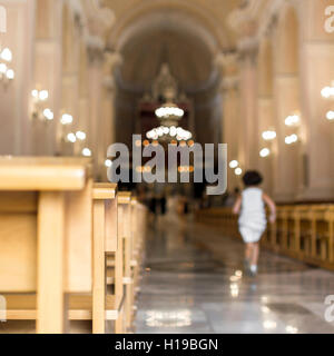 Une petite fille s'exécute à l'église, en direction de l'autel. Arrière-plan flou flou artistique. Banque D'Images