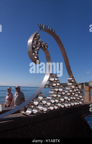 À midi, sur l'équinoxe d'automne, les gens profitent d'un soleil glorieux sur le front de mer à la sculpture sur vagues, Seaton, à Devon. Banque D'Images