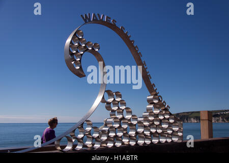 À midi, sur l'équinoxe d'automne, les gens profitent d'un soleil glorieux sur le front de mer à la sculpture sur vagues, Seaton, à Devon. Banque D'Images