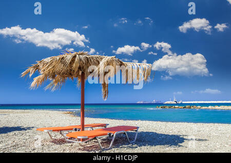 Parapluie de paille sur une plage de sable à la Grèce. Chaises de plage avec parasols sur une magnifique plage à l'île de Crète. Banque D'Images