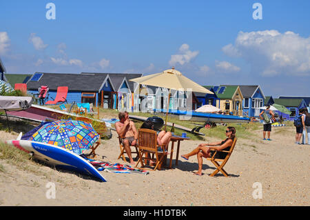 Vacanciers assis dans des chaises longues devant des cabanes de plage sur les bancs de sable de Mudeford, Hengistbury Head Banque D'Images