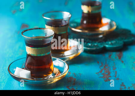 Du thé turc servi en verre en forme de tulipe avec deux petits morceaux de sucre sur une soucoupe sur la table rustique bleu Banque D'Images
