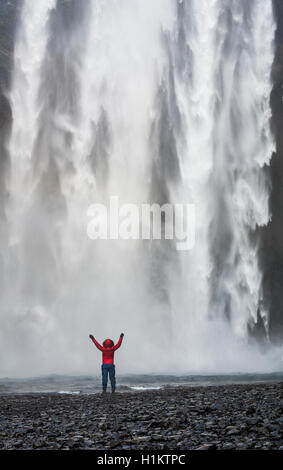 Randonneur avec bras tendus devant la cascade Skógafoss en hiver, Skógar, Région du Sud, Islande Banque D'Images
