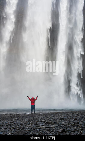 Randonneur avec bras tendus devant la cascade Skógafoss en hiver, Skógar, Région du Sud, Islande Banque D'Images