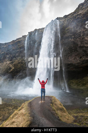 Randonneur avec bras tendus en face de la cascade de Seljalandsfoss, rivière Seljalandsá, Région du Sud, Islande Banque D'Images