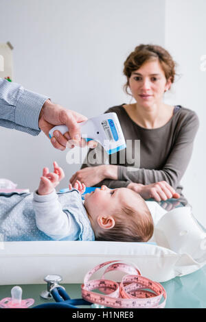 Contrôle de la température d'un bébé de trois mois fille avec thermomètre frontal. Banque D'Images