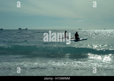 Stand up Paddling paddleboarders sur leurs genoux Plage de Gyllyngvase, Falmouth, Cornwall avec des navires-citernes dans le lointain Banque D'Images