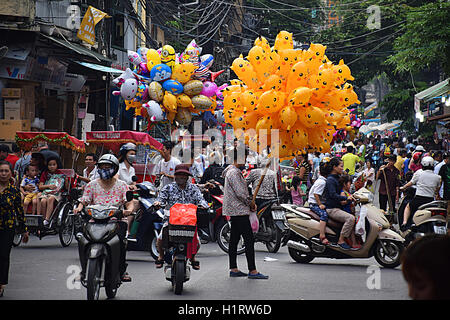 Vendeur de ballons, des motos et des foules dans les rues animées de la vieille ville de Hanoi, Vietnam Banque D'Images