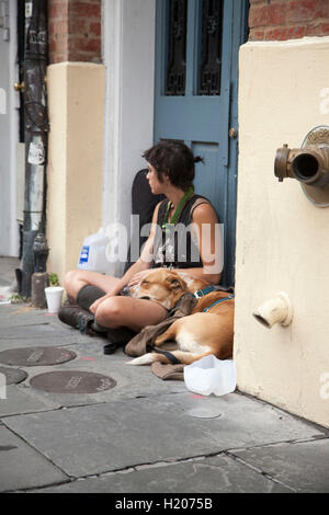 Une femme assise sur la rue en face de la baie de porte dans le quartier français de La Nouvelle-Orléans, accompagnée par son chien. Banque D'Images