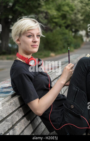 Portrait de jeune femme avec un casque s'appuyant sur banc de parc Banque D'Images