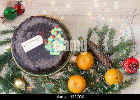 Sur la table en bois sont des cadeaux de Noël : délicieux gâteau au chocolat, mandarine, décorations pour arbres de Noël. Banque D'Images