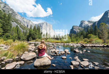 Jeune femme assise sur des pierres dans la rivière Merced, vue sur la vallée, vue d'El Capitan, Yosemite National Park, California, USA Banque D'Images