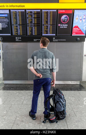 Un jeune homme à la recherche d'un conseil de départ, l'aéroport de Heathrow, Londres, UK Banque D'Images