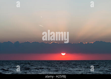 Météo, le lever du soleil sur la mer, manche à Broadstairs. Ciel rouge avec Sun sur le point de disparaître derrière cloud après avoir augmenté. Couche de nuages au-dessus, le motif des rayons de tournage. Banque D'Images