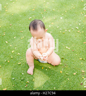 Outdoor portrait of Asian baby boy jouer assis et en se déplaçant sur le terrain d'herbe verte dans le parc Banque D'Images