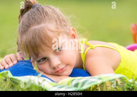 Fille de cinq ans se trouve sur un lit sur un pré vert et bien regarde de côté Banque D'Images