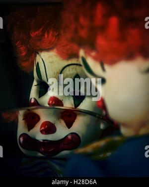 Un gros plan d'un clown maléfique effrayant à la poupée jouet dans un miroir brisé qui pourrait être possédé par le mal pour une Halloween. Banque D'Images
