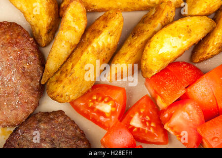 Gros plan des hamburgers avec les quartiers de pommes de terre et de tomate fraîche sur une plaque Banque D'Images