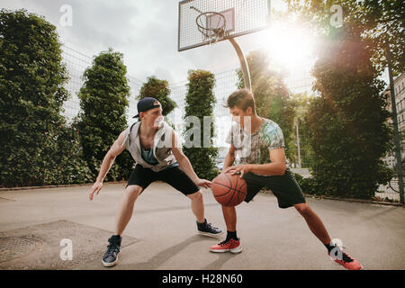 Amis adolescents jouer streetball les uns contre les autres et s'amuser. Deux jeunes hommes ayant un match de basket-ball extérieur sur cour Banque D'Images