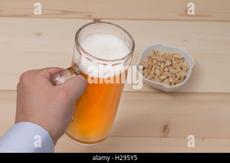 Homme main tenant une chope de bière pression. Cacahuètes dans le bol sur la table. Banque D'Images