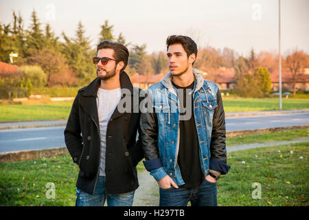 Deux beaux jeunes hommes à la mode décontractée, 2 amis, dans un parc urbain de marcher et de parler ensemble Banque D'Images