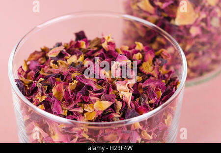 Des pétales de rose dans un bol en verre sur fond rose. Fleurs séchées, utilisées pour des parfums, des cosmétiques, du thé et des bains. Banque D'Images