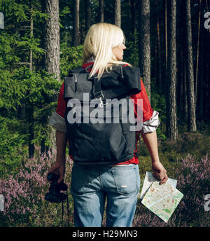 Jeune femme active'debout dans une clairière dans les bois avec un sac à dos, jumelles et d'un holding à la carte et à la forêt. Mode de vie sain et actif. Banque D'Images