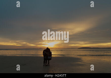 Couple multiracial regardant le coucher du soleil sur la plage Banque D'Images