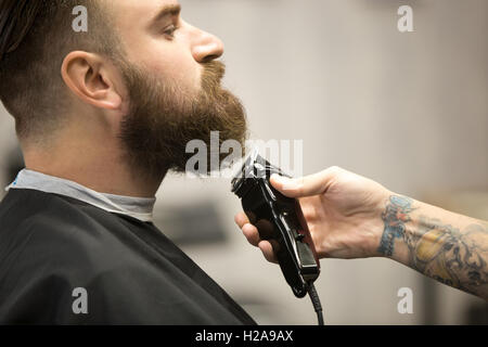 Close-up side view portrait of handsome young bearded caucasian man getting beard en toilettage barbershop moderne. Coiffure wit Banque D'Images